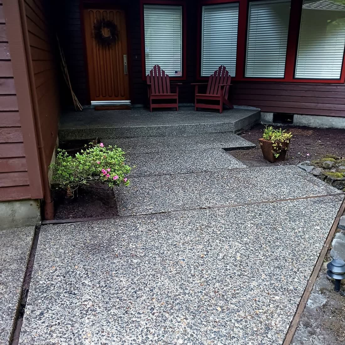 A clean exposed-aggregate walkway leading to a front door and two red chairs.