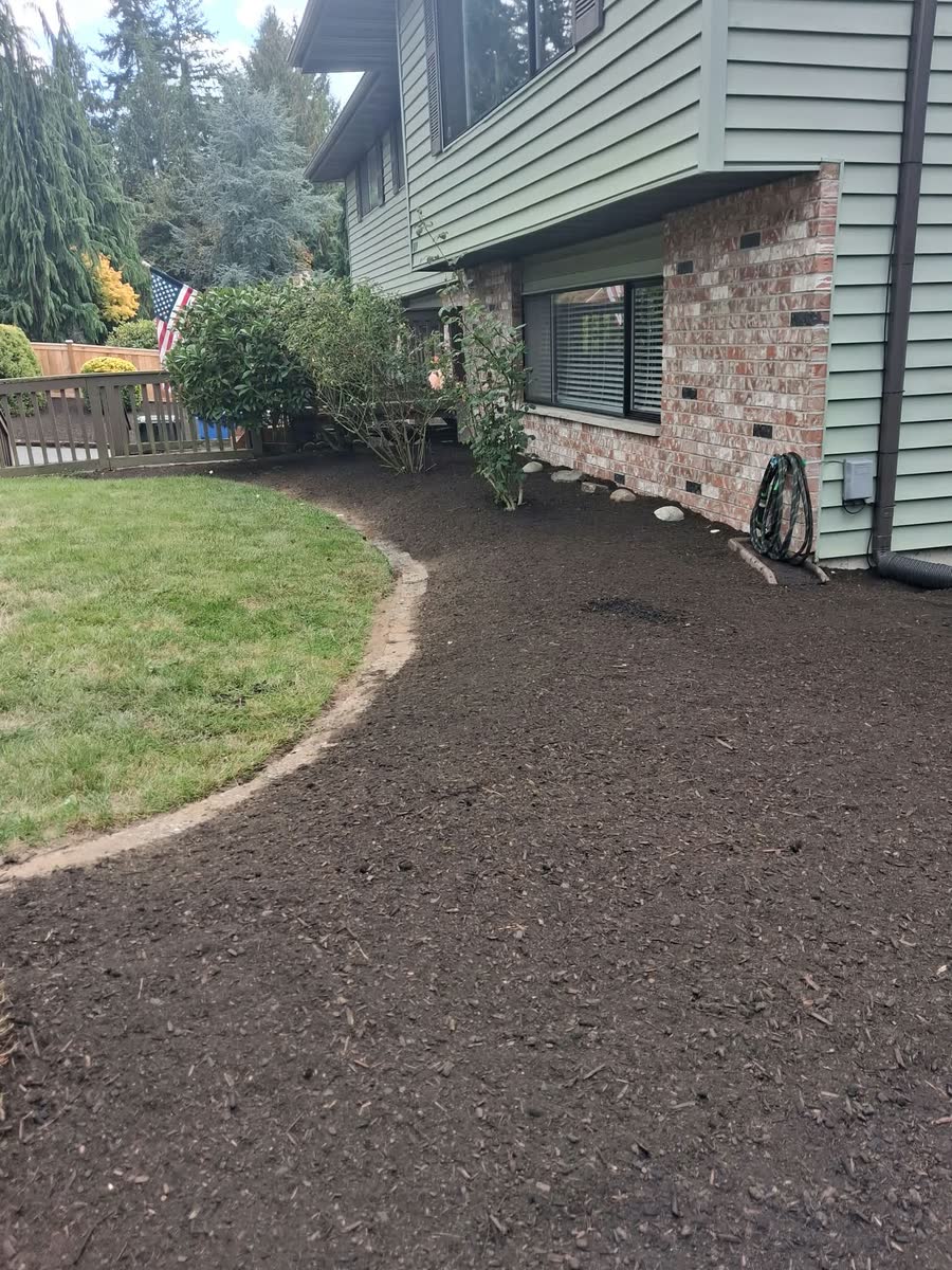 A fresh bed curving along a lawn edge beside a brick and siding house.