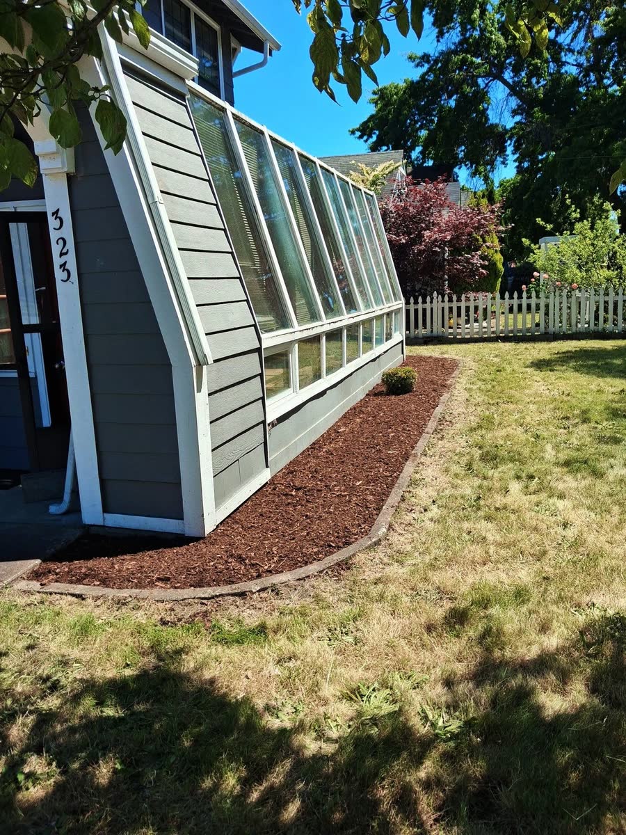 A fresh bark bed along a glass sunroom wall and a cut lawn.