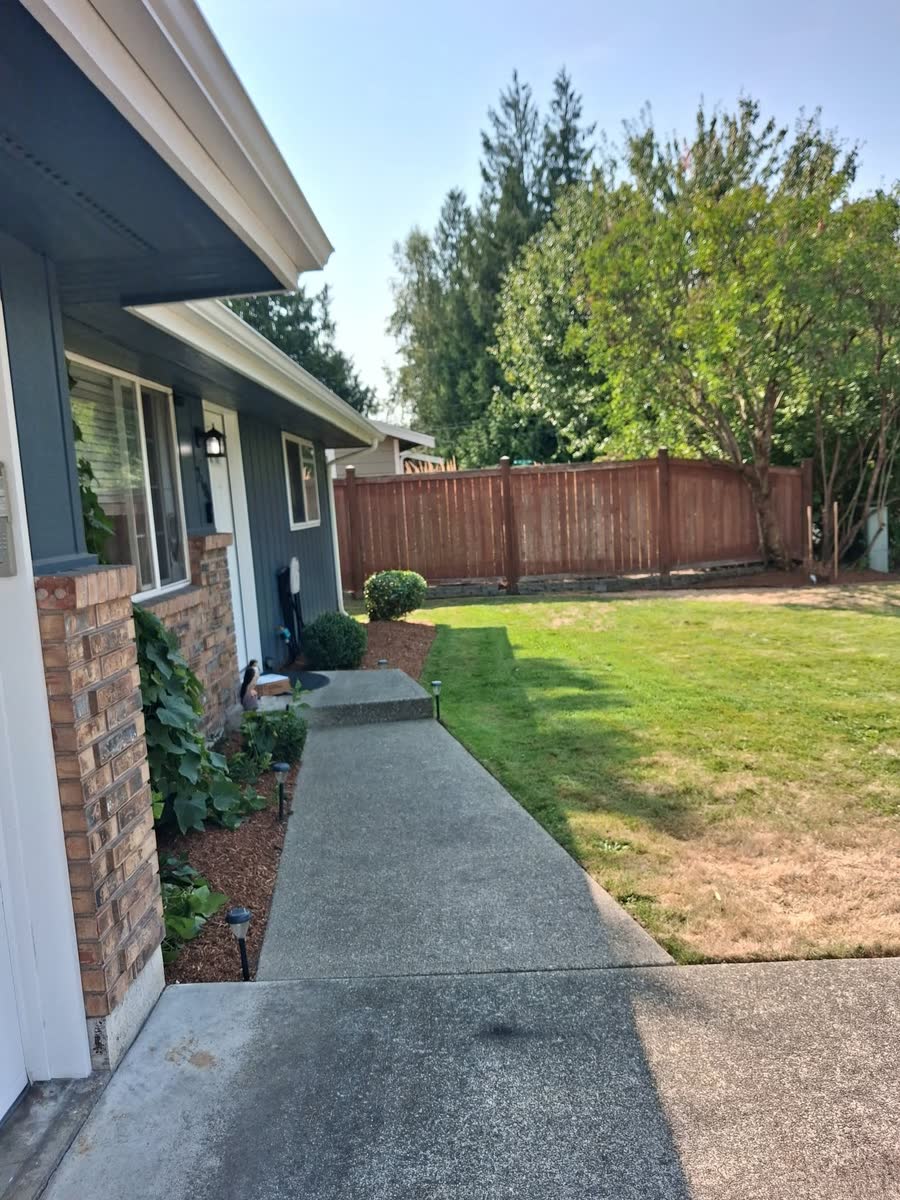 A clean concrete path beside a cut green lawn and a wooden fence.