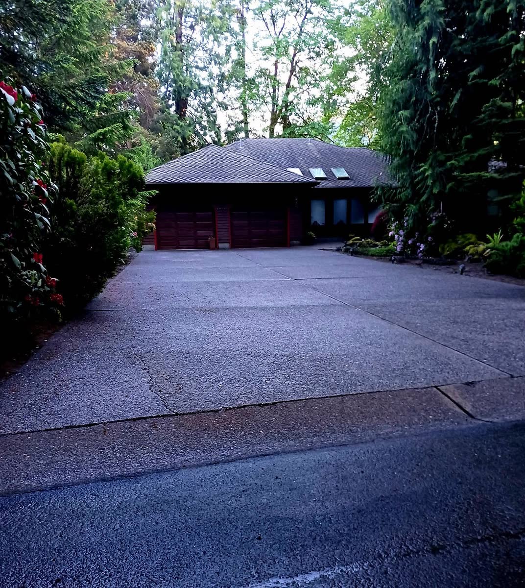 A clean dark driveway in front of a wood-sided house in the trees.